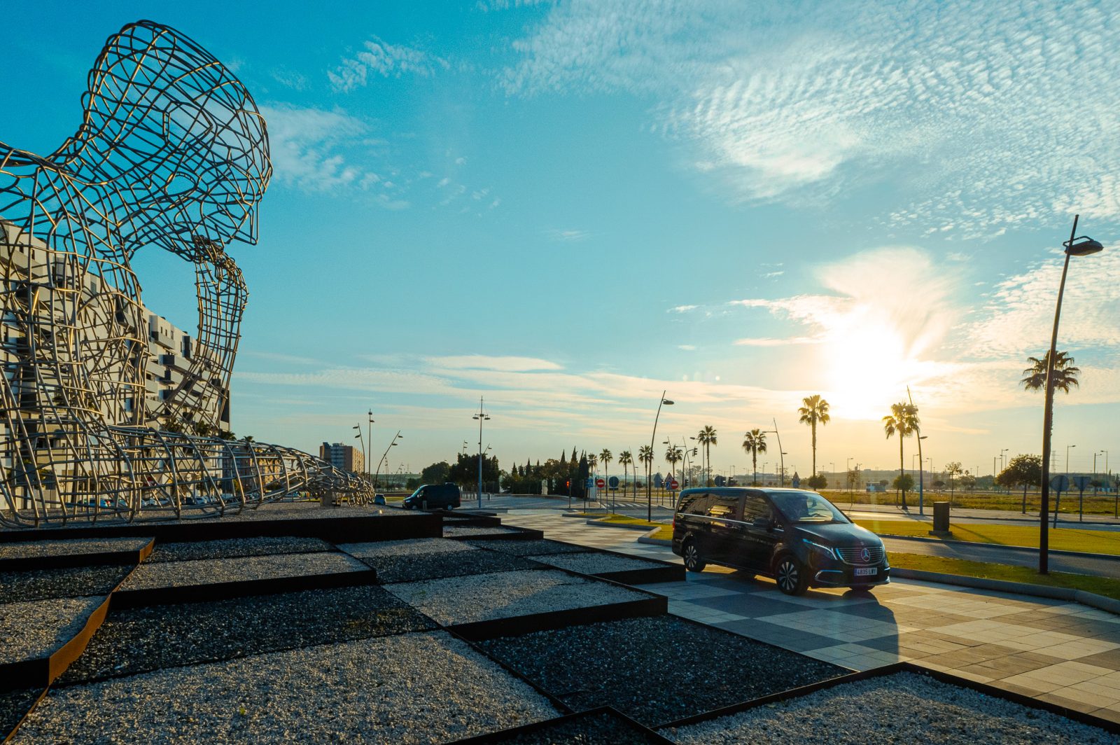 Escultura metálica gigante al atardecer con palmeras