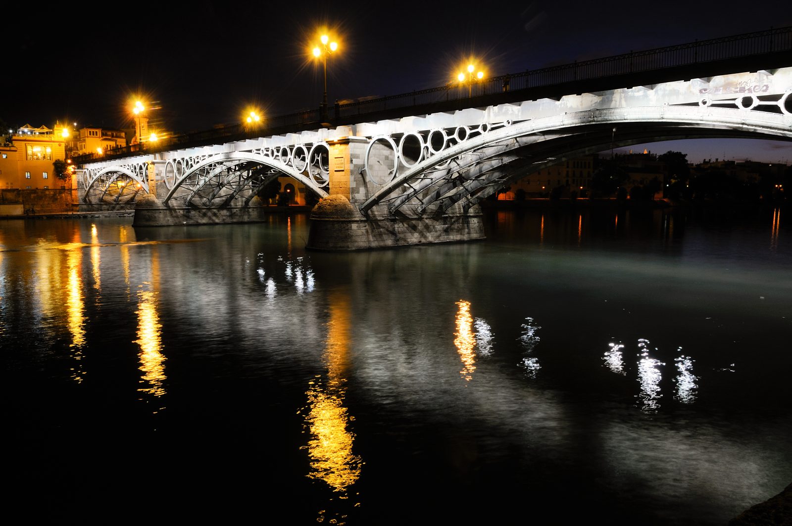 Puente iluminado sobre río de noche en Sevilla